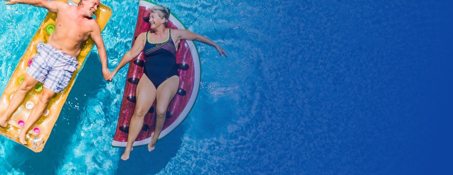 Above vertical view of people old senior couple taking hands with love and having fun on the blue clear swimming pool together enjoying the summer holiday vacation with trendy coloured lilos inflatable mattress