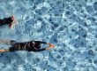 Two boys funny swimming together in clear water pool, taken from aerial view.